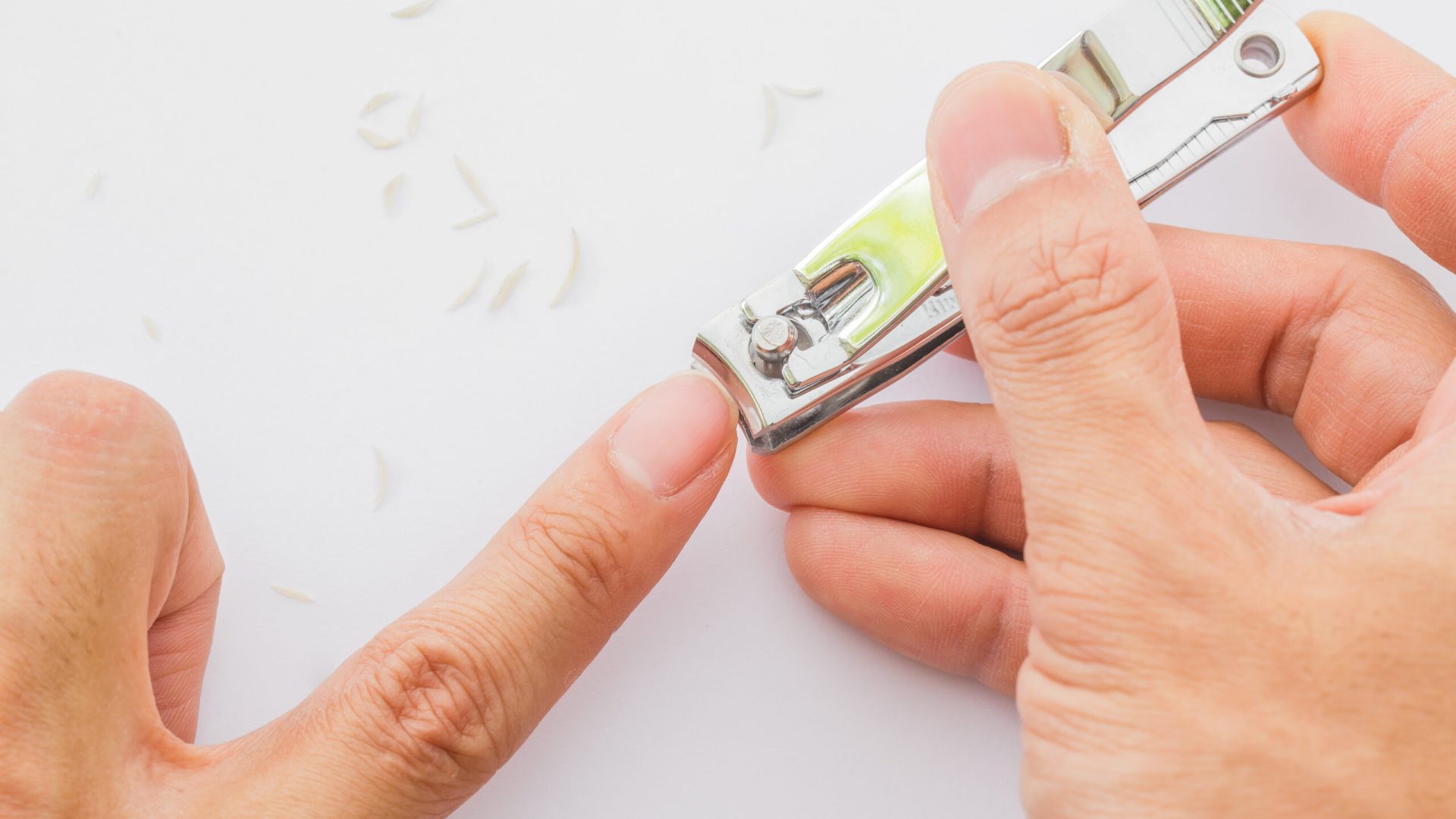 Man,Cuts,His,Nails,With,Tweezers,On,A,White,Background.